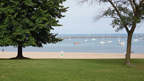 The lake bluff at South Shore Park, a sandy beach and lawn framing open water and moored sailboats.