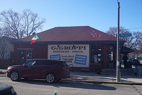 G. Groppi Food Market, a one storey red brick corner store with its name and goods painted directly onto the brick, flags over the entrance.