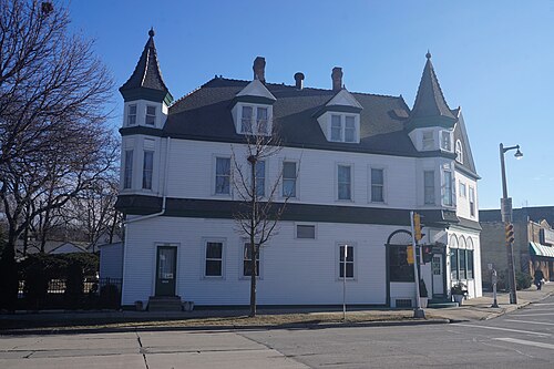 A three storey white building with two corner turrets and a ground floor storefront, at a Kinnickinnic Avenue intersection.