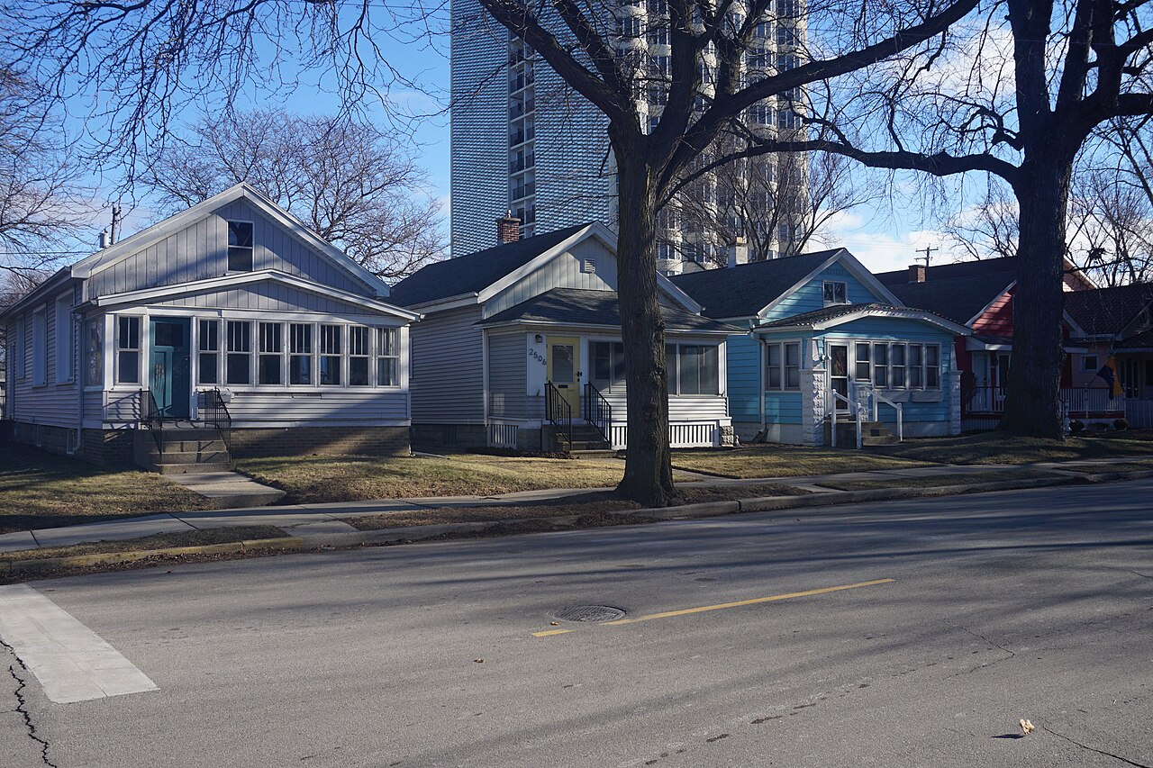 One storey gable roofed frame cottages in different colors along South Superior Street, an apartment tower rising behind the block.