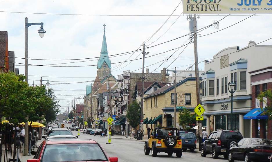Brady Street looking west toward St. Hedwig's steeple in the distance, storefronts and awnings lining both sides, a Food Festival banner strung over the street.