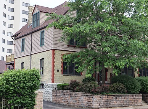 The George W. Peck Row House on North Farwell Avenue, a Queen Anne building with a brick ground floor and ornamental wood shingling above, a hedge and low stone wall along the sidewalk.