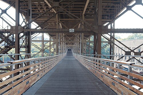 The wood decked footbridge slung beneath the Holton Street Viaduct, plank flooring and timber handrails running between the steel trusses overhead.
