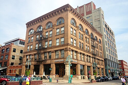 A five storey red brick warehouse wrapping a street corner, with a loading dock awning and a decorative street sign pole at the curb.