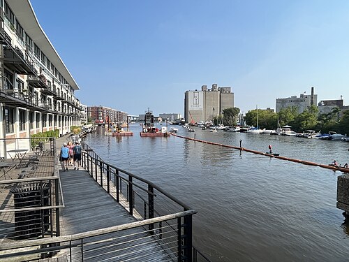 A disused steel railway swing bridge standing mid channel in the Milwaukee River, its control cabin still perched on a stone pier, brick lofts and small boats along the banks.