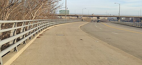 The Hank Aaron State Trail's paved path and metal railing running beside Canal Street, a road viaduct and a high rise ahead in the distance.