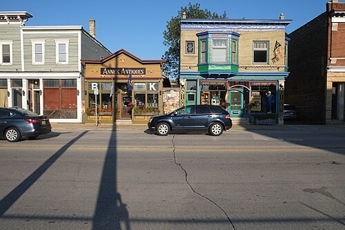 Annex Antiques and Clinton Street Antiques storefronts side by side, one in dark wood signage under a peaked roof, the other in cream brick with green and blue trim and a corner oriel window.