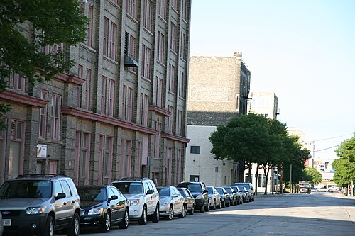 A row of tall cream brick industrial buildings on Florida Street, pink painted window trim and a faded painted wall sign, cars parked along the curb.