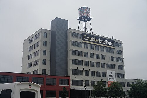 The Coakley Brothers building, a white painted concrete factory front with a rooftop water tower sculpture on steel legs above the Coakleybrothers sign.