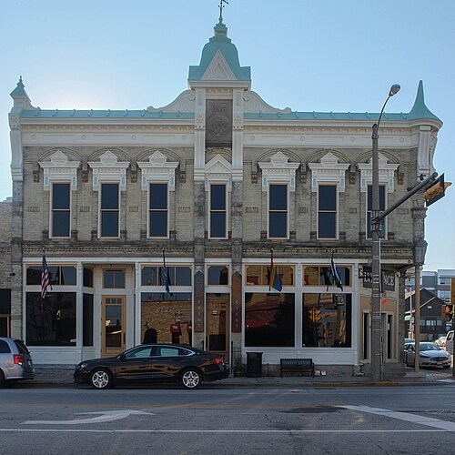 The Bahr Building's cream brick front, a corner turret on a cast iron column and a central cupola with a weathervane, storefront windows below with a rainbow flag hanging in one.